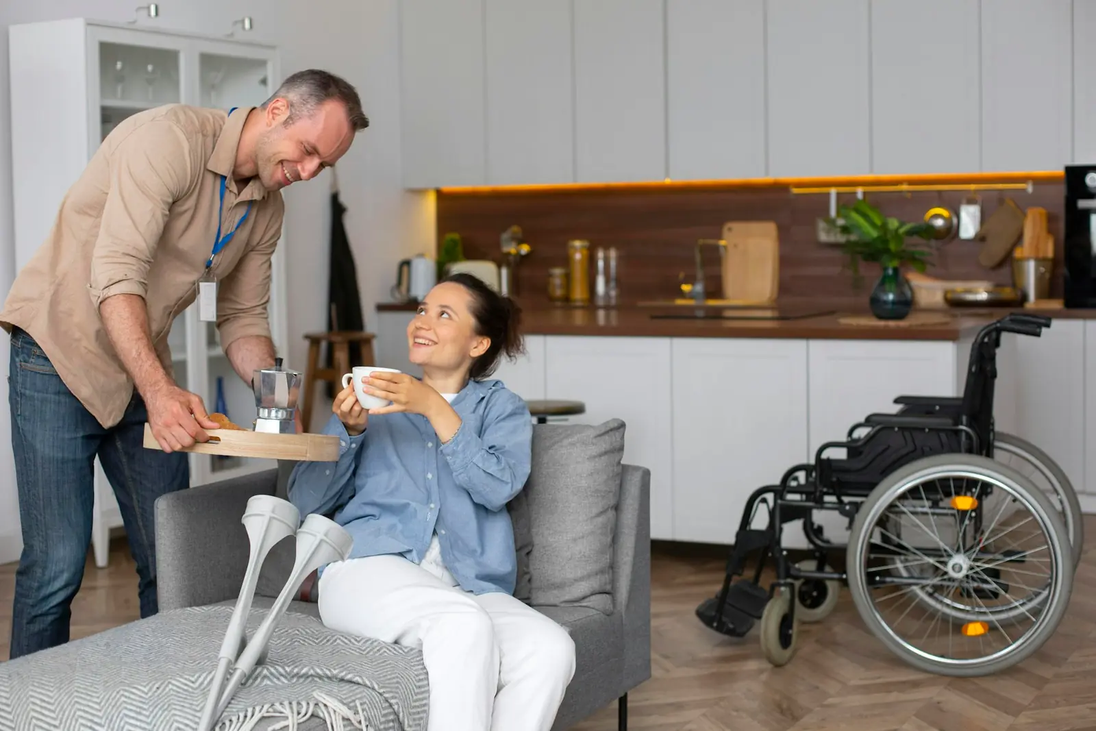 A support worker bringing a tray to a woman on her sofa, with her wheelchair nearby